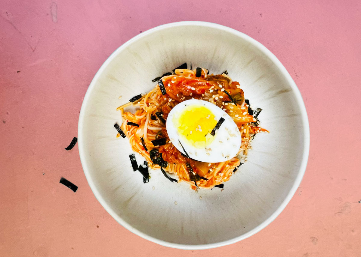 Kalte Kimchi Guksu Nudeln in einer Schüssel mit Gurke, Frühlingszwiebeln und Sesam